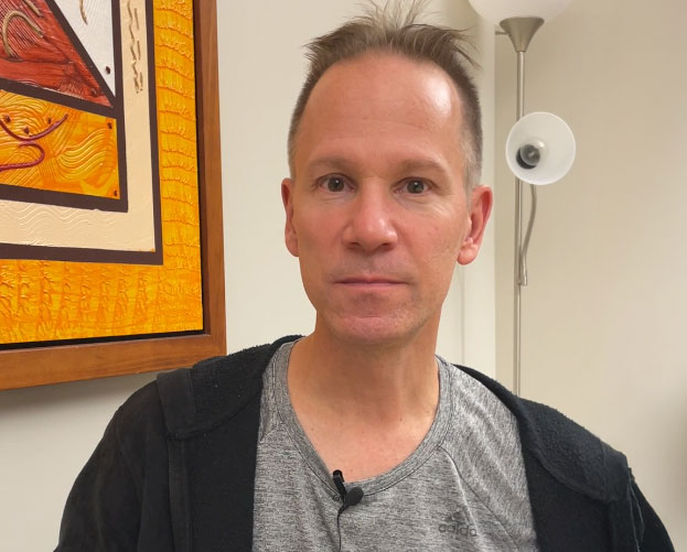 Un homme assis regarde la caméra.