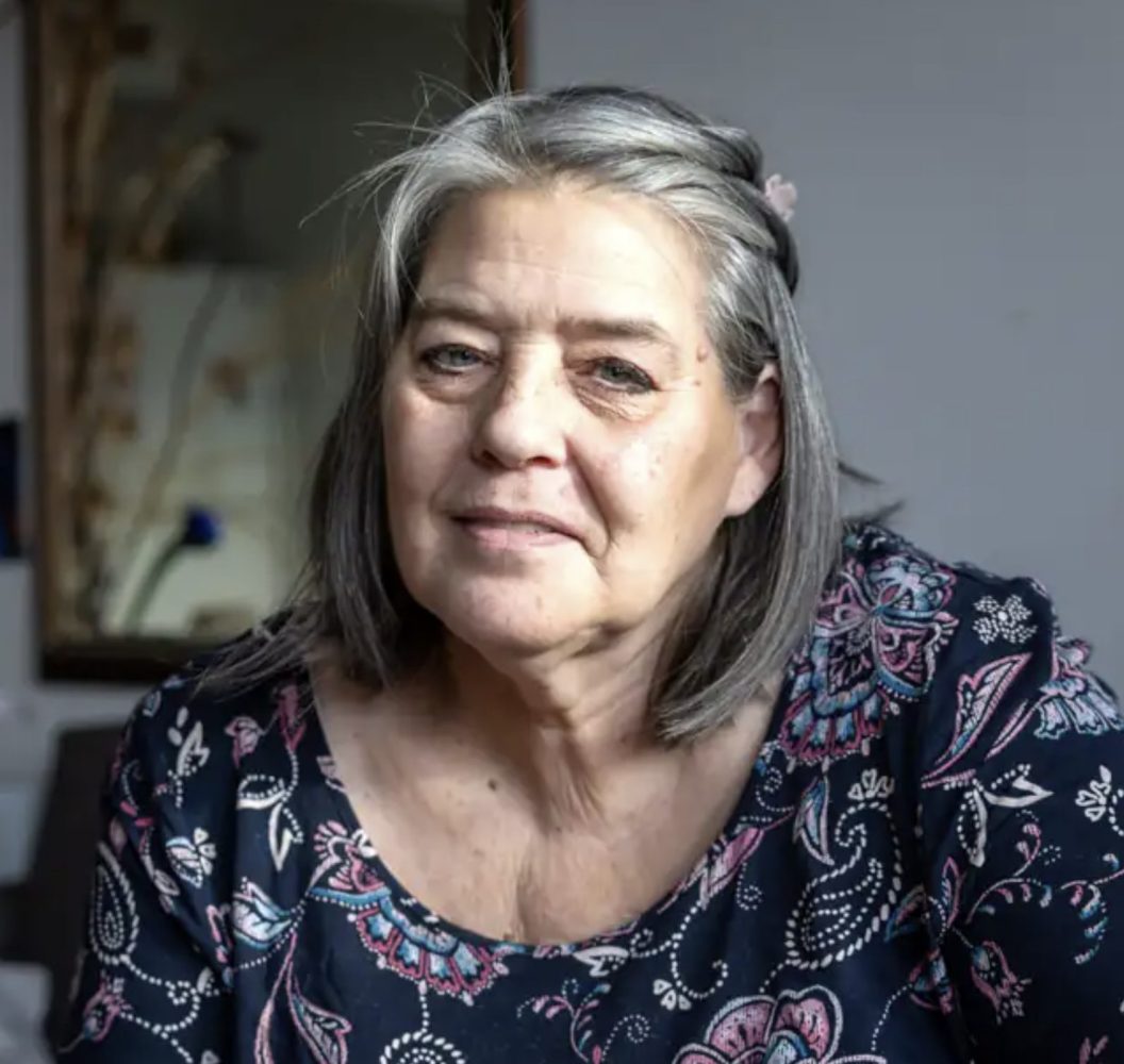 Une femme âgée assise regarde la caméra.